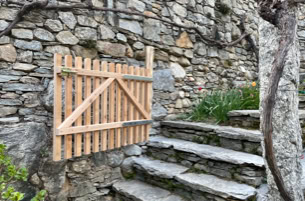 Ein massgefertigtes Garten aus Lärchenholz montiert an einer Trockensteinmauer inmitten der Tessiner Rebbergen