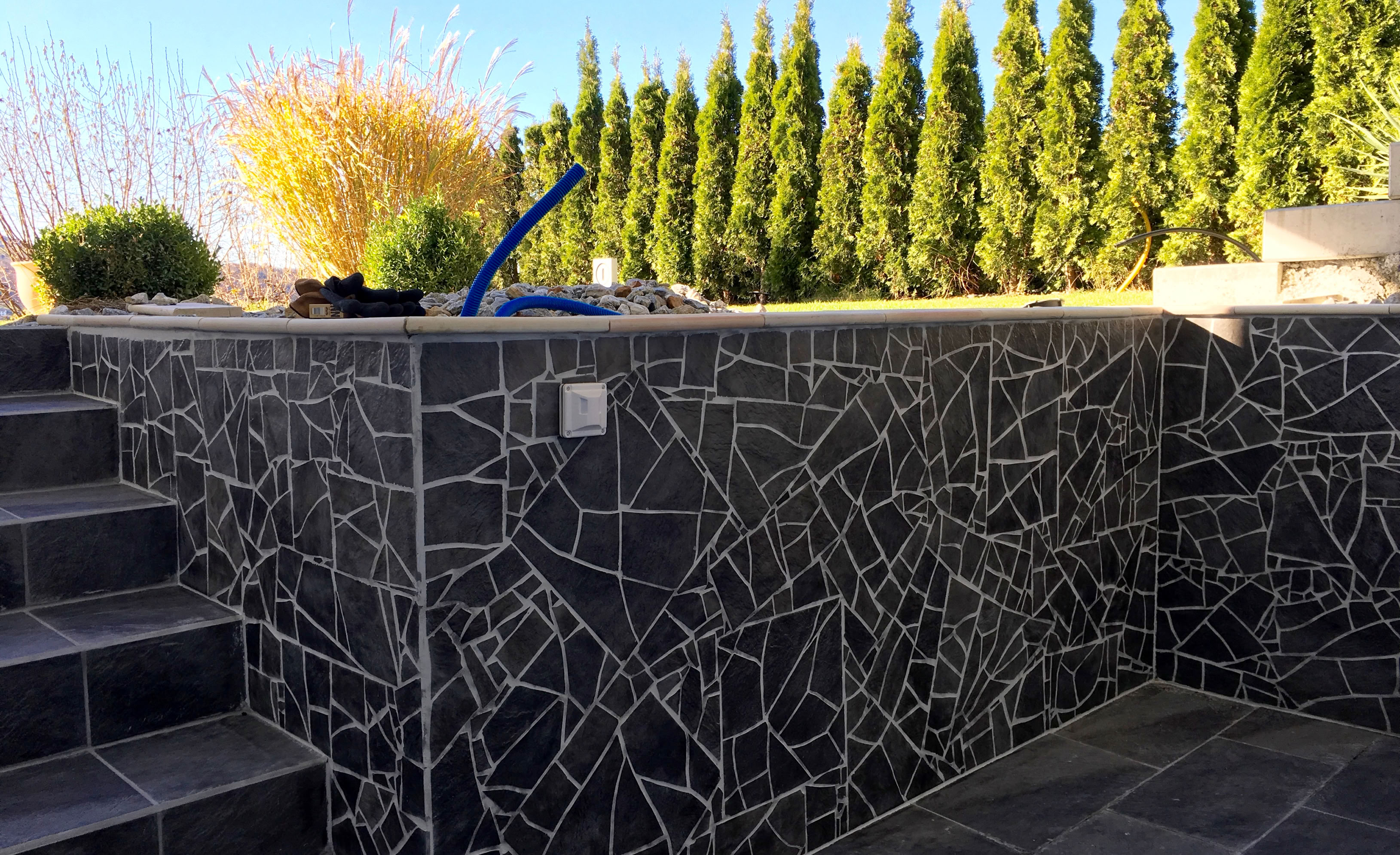 Steinmauer mit verspieltem Fliesenmosaik.